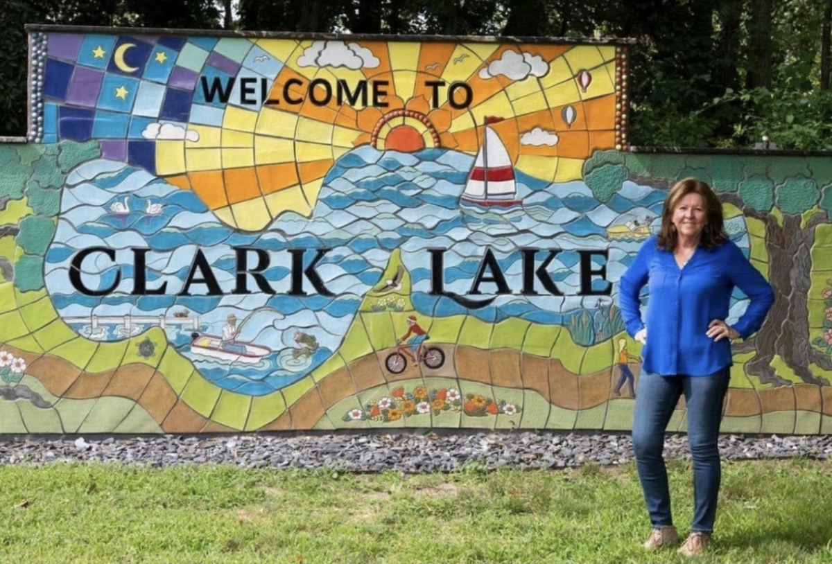 Owens Community College Artist in Residence. Annette Fink stands in front of a mural created for Clark Lake. She is the Summer 2024 Artist in Residence at Owens Community College.